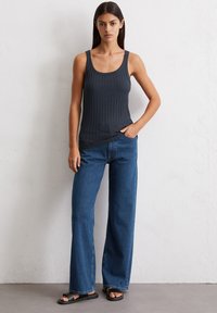 Szara ryflowana bluzka na ramiączkach z szerokimi paskami, połączona z niebieskimi, wysokimi dżinsami z szerokimi nogawkami. Model nosi czarne płaskie sandały. Prosty design, codzienny wygląd.