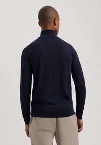 Maglione in maglia blu navy con colletto alto, polsini e orlo a coste. Tessuto morbido e design aderente, che si abbina a pantaloni beige chiaro.