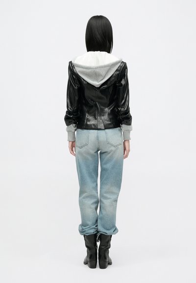 Μαύρο συνθετικό δερμάτινο τζάκετ με γκρίζα κουκούλα, συνδυασμένο με ανοιχτό μπλέ φαρδιά τζιν παντελόνια. Μαύρες μπότες ολοκληρώνουν την εμφάνιση. Διακοσμημένο με πτυχώσεις στους μανικιού.