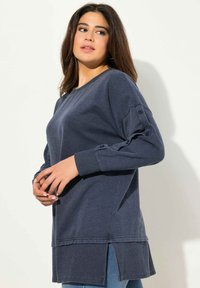 Maglietta a maniche lunghe blu navy con vestibilità comoda, polsini a coste, dettagli con bottoni sulle maniche e spacchi laterali per facilità di movimento.
