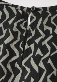 Schwarz- und cremefarbenes geprägtes Stoffmuster mit Zickzackdesign. Verfügt über einen kleinen Knopfverschluss auf der Rückseite und eine Schlüssellochöffnung. Weiche Textur.