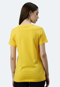 T-shirt gialla a maniche corte realizzata in un tessuto morbido ed elastico. Presenta un classico colletto a giro e una silhouette aderente.