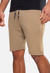 Shorts côtelés beiges avec une taille élastique et un cordon de serrage. Dotés de poches latérales et d'une coupe droite se terminant au-dessus du genou.