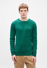 Πράσινο πουλόβερ με πλέξιμο, στρογγυλή λαιμόκοψη, ραμμένα μανίκια και στρίφωμα, με μικρό λογότυπο στο στήθος.