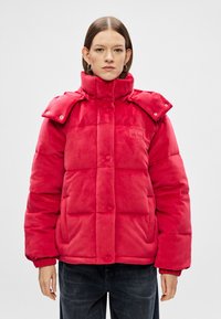 Sarkanais pīlāju mētelis ar augstu apkakli, snap pogām, sānu kabatām un gludu tekstūru. Ar plecu epauletēm un logotipa detaļām.