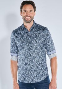 Hemd mit Knöpfen aus marineblauem Stoff, das ein florales Muster in Hellblau und Weiß aufweist. Hochgerollte Ärmel mit kontrastierenden Manschetten.