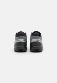 Pantofi sport negri și gri cu o parte superioară din plasă, design texturat și un model pronunțat pe talpă. Prezintă marca 'SALOMON' pe laterale.