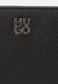 Schwarze, strukturierte Lederbörse mit einem silbernen "HUGO"-Logo. Die Oberfläche hat eine genoppte Struktur, die den Griff verbessert und die Haltbarkeit erhöht.