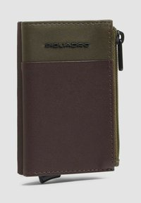 Bruine en olijfgroene lederen portemonnee met een ritssluiting voor munten, Piquadro-logo, verticaal ontwerp, gladde textuur en contrasterende kleurvlakken.