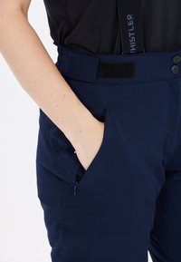 Marinblå vattentäta byxor med slät yta, två sidofickor och justerbart velcro midjeband. Har logo på sidan.