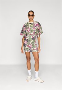 Φόρεμα με λουλουδάτο μοτίβο και κοντά μανίκια, διακοσμημένο με ροζ λουλούδια και πράσινα φύλλα σε μπεζ φόντο, συνδυασμένο με γυαλιά ηλίου και αθλητικά παπούτσια.