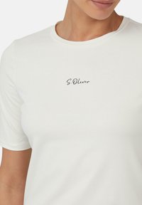 Biała koszulka z krótkim rękawem, wykonana z miękkiego materiału, z okrągłym dekoltem i czarnym, kursywnym logo "S.Oliver" na piersi.