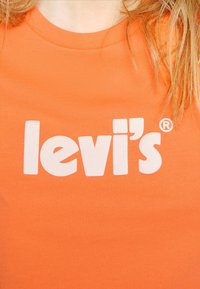 Camiseta de algodón naranja con un diseño de logo blanco de "levi's" con un símbolo de marca registrada, cuello redondo y mangas cortas.