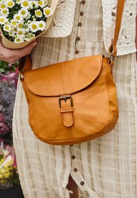 Brown leather crossbody bag with a rounded shape, flap closure, and a decorative buckle. Smooth texture with visible stitching details.