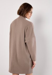 Abito a maglia beige a coste con colletto alto e maniche lunghe, caratterizzato da un fit morbido e spacco laterale per una maggiore libertà di movimento.