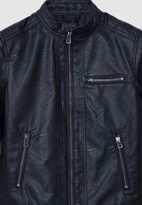 Czarna skórzana kurtka z wysokim kołnierzem, zamek błyskawiczny z przodu oraz trzema kieszeniami na zamek. Posiada pikowane wykończenia na ramionach.