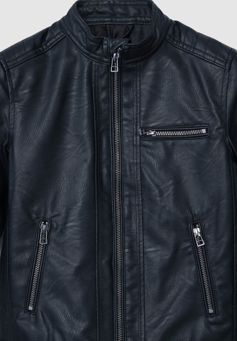 Czarna skórzana kurtka z wysokim kołnierzem, zamek błyskawiczny z przodu oraz trzema kieszeniami na zamek. Posiada pikowane wykończenia na ramionach.