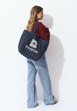Bolso tote a cuadros en azul marino y verde con un logotipo en gris claro "Brownie". Cintas anchas y tejido suave y texturizado. Diseño de larga caída, aspecto casual.