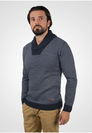 Pulover bleumarin cu un model texturat țesut, având un guler tip șal și manșete nervurate. Include un mic patch cu logo în partea de jos.