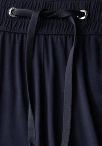 Marineblauwe sweatpants met een elastische tailleband, voorzien van een trekkoord met zilverkleurige hardware, en een zachte textuur. Close-up weergave.