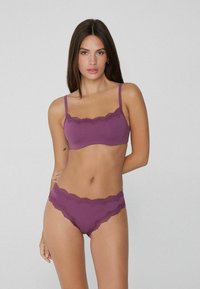 Fialový prádlo sestava s braletkou s vlnitým krajkovým lemem a odpovídajícími vysokými kalhotkami s podobným krajkovým detailem, hladká textura.