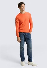 Bright orange long-sleeve sweater, slim fit, paired with blue jeans and white sneakers. Smooth texture and simple design.