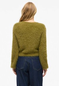 Olivgrüner, flauschiger Pullover mit langen Ärmeln und rundem Ausschnitt. Das Material ist weich und strukturiert, mit einem kürzeren Saum.