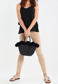 Borsa tote intrecciata nera con accenti in pom-pom testurizzati sulla parte superiore, manici robusti e un design spazioso e strutturato.