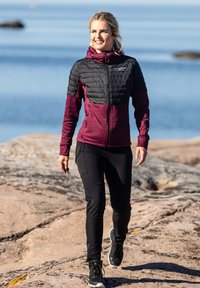 Dark maroon and black zip-up jacket with quilted texture on shoulders, paired with black pants and black sneakers, worn by a woman outdoors.