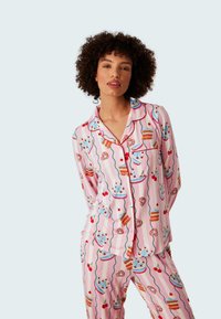 Rosa pyjamaset med ett lekfullt dessertmönster med tårtor, körsbär och glasyr. Mjukt tyg, långa ärmar och kontrasterande detaljer.