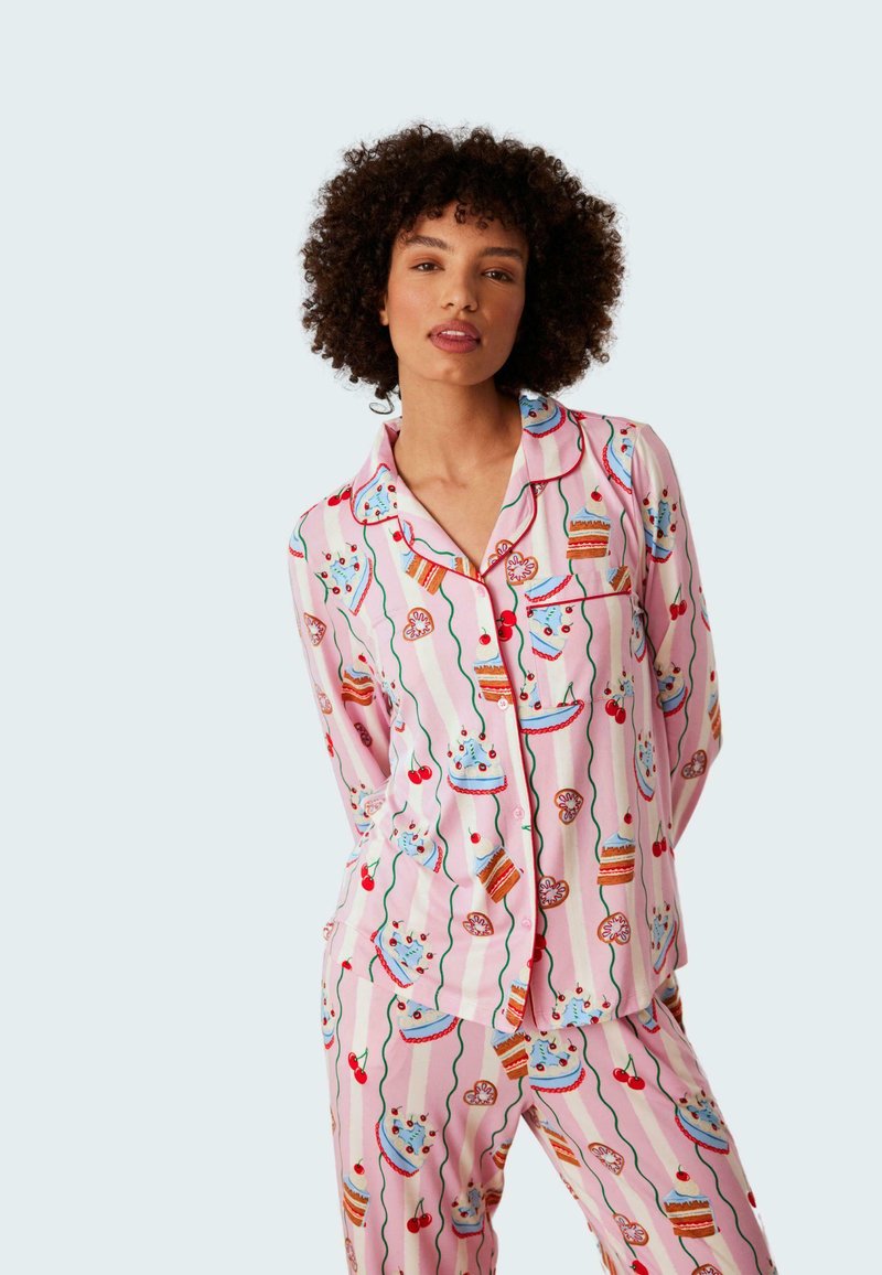 Rosa pyjamaset med ett lekfullt dessertmönster med tårtor, körsbär och glasyr. Mjukt tyg, långa ärmar och kontrasterande detaljer.