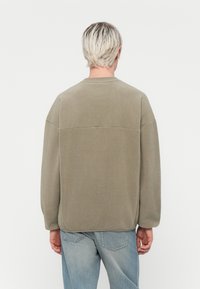 Olivenfarget fleecegenser med rund hals, senkede skuldre og en horisontal søm over ryggen. Myk tekstur og løs passform.