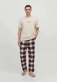 Béžové bavlnené tričko s logom a kárované pyžamové nohavice v námorníckej modrej, červenej a bielej farbe. Nohavice majú elastický pás a bočné vrecká.