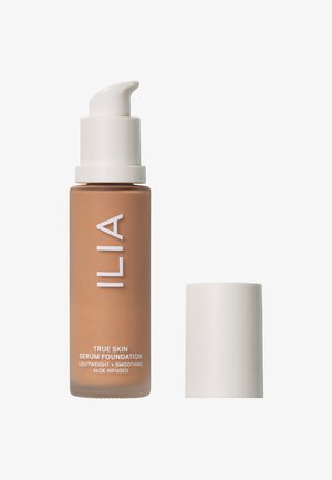 ILIA True Skin Serum Foundation i en brun glasflaska med ett vitt pumplock; texten på flaskan indikerar att den är lätt och innehåller aloe.
