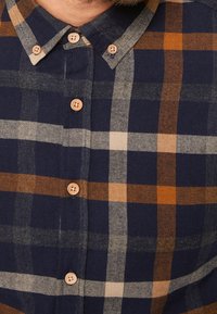 Camicia scozzese blu navy con motivo a spina di pesce, con accenti arancioni, beige e grigi, e bottoni in legno. Tessuto dalla trama morbida.