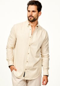 Langärmliges, cremefarbenes Leinenhemd mit Knopfkragen, verdeckter Knopfleiste und abgerundetem Saum. Hat eine dezente Textur und kontrastierende Nähte.