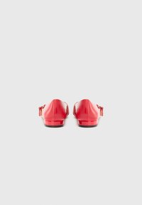 Chaussures rouges brillantes vues de l'arrière, avec un petit talon et des lacets décoratifs, sur fond gris uni.