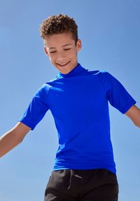 Modra kratka majica za zaščito pred draženjem z visokim ovratnikom, narejena iz gladkega, raztegljivega materiala, tesno oprijema trup in roke.