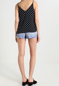 Svart och vit prickig tanktop med V-ryggdesign, tillsammans med ljusblå slitna jeansshorts och svarta slip-on skor.