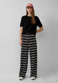 Czarny sweter z krótkim rękawem w połączeniu z szerokimi spodniami w duże białe kropki, uzupełniony różową czapką z napisem.