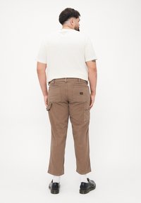 Brown cargo pants with multiple pockets, a relaxed fit, and a slightly tapered leg; worn with a cream T-shirt and black shoes.
