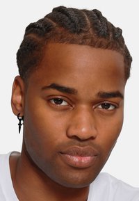 Zwarte man met gevlochten haar en een zwarte oorbel. Hij draagt een wit shirt. De achtergrond is eenvoudig en neutraal van kleur.