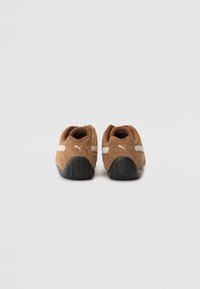 Braune Wildledersneaker mit einer strukturierten schwarzen Gummisohle, die mit einem weißen Streifenakzent und goldener Markenprägung an der Ferse ausgestattet sind.