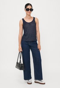 Un débardeur bleu foncé avec un léger éclat, associé à un jean large taille haute. Les accessoires comprennent un sac à main noir et des lunettes de soleil.