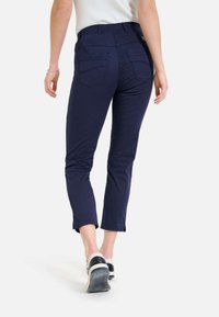 Marineblaue Baumwollmischung cropped Hose mit Gesäßtaschen, schmaler Schnitt und Saum, der über dem Knöchel endet, kombiniert mit lässigen Sneakers.