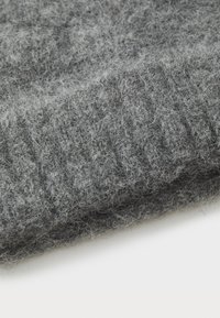 Sivi pleteni materijal, koji se odlikuje mekanom, pahuljastom teksturom s rebrastim uzorcima. Materijal izgleda debeo i topao. Presavijen s vidljivim nitima i vlaknima.
