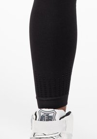 Črne športne leggins hlače s teksturiranimi ventilacijskimi paneli blizu roba in prilagojenim silhueto, v kombinaciji z belimi supergami v visoki različici.
