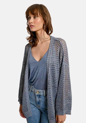 Cardigan grigio leggero e a maglia aperta con maniche lunghe, polsini a coste e una vestibilità ampia, abbinato a una maglietta blu a scollo a V e jeans.