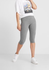 Szare legginsy capri wykonane z elastycznej tkaniny, charakteryzujące się dopasowanym krojem i długością do kolan, zestawione z białym crop topem z grafiką oraz białymi sneakersami.