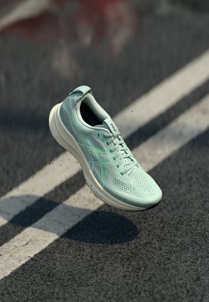 Light green athletic shoe with a mesh upper, visible lacing, and contrasting white sole, shown in mid-air above a dark, textured surface.